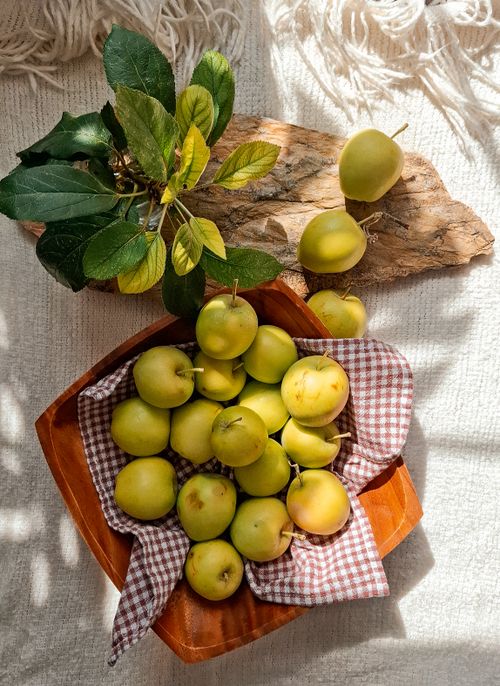 Free A cozy arrangement of green apples on a wooden tray with checkered cloth. Stock Photo