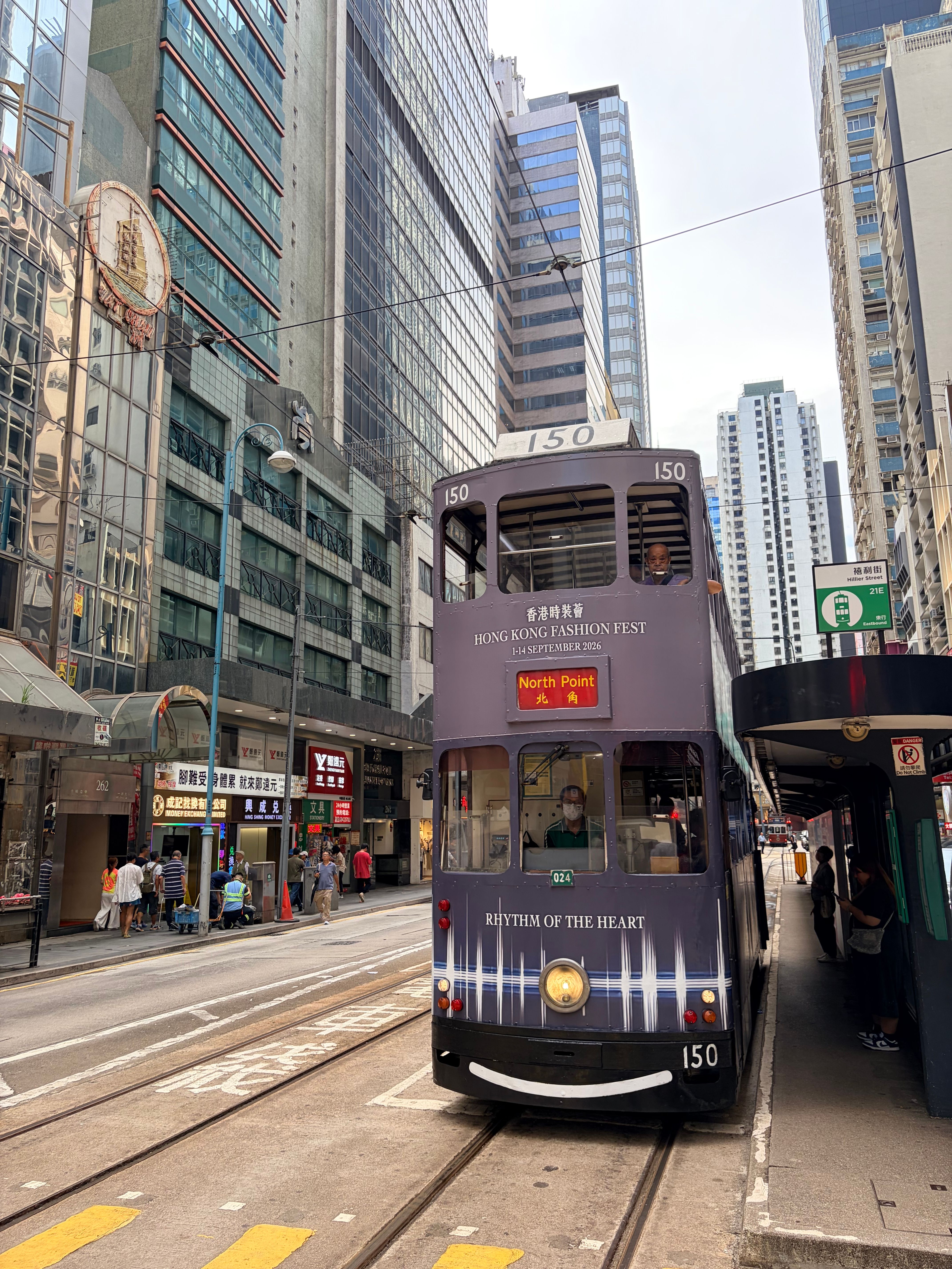 Double-decker tram on a bustling Hong Kong street amidst tall skyscrapers, capturing urban life.