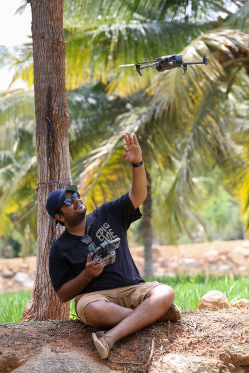 Free Man sitting under palm trees controlling a drone with a remote. Stock Photo