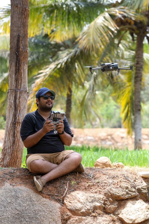 Free Man sitting outdoors controlling a drone with a remote in a tropical park area. Stock Photo
