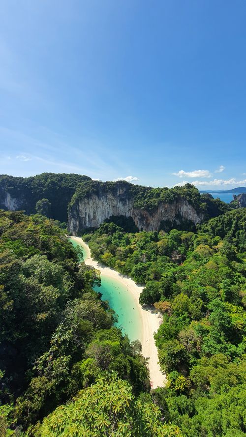 Free A stunning aerial shot of a secluded tropical beach surrounded by lush greenery and cliffs under a clear blue sky. Stock Photo