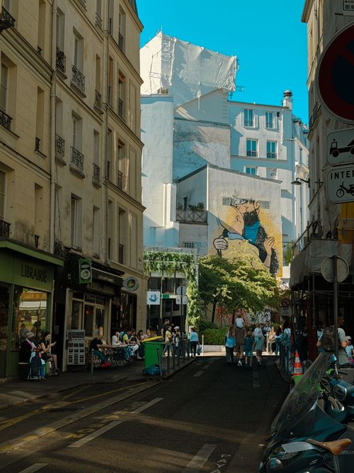 Free Vibrant Paris street view with outdoor cafes and a colorful mural under clear blue skies. Stock Photo