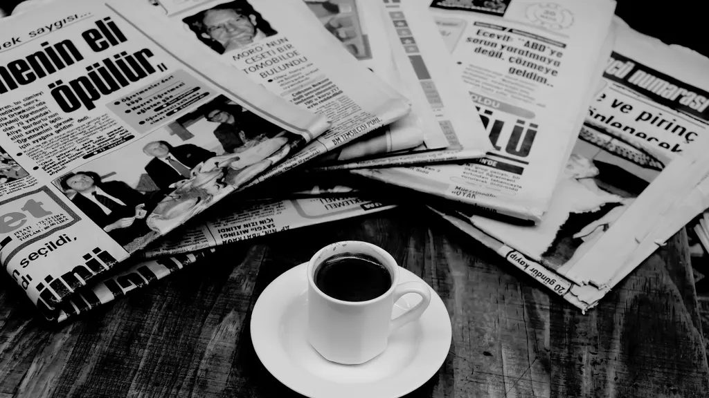 Coffee cup beside a stack of folded newspapers on a wooden table