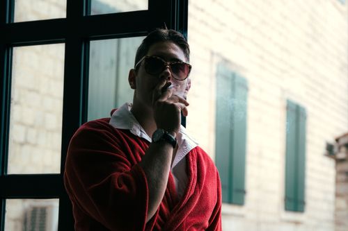 Free A man in a red robe smokes near a window, exuding a relaxed and mysterious vibe. Stock Photo