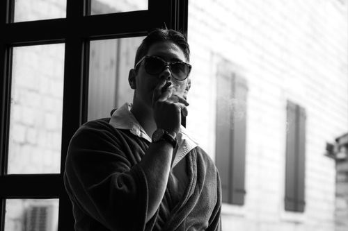 Free Stylish man in sunglasses enjoying a cigar indoors, captured in black and white photography. Stock Photo