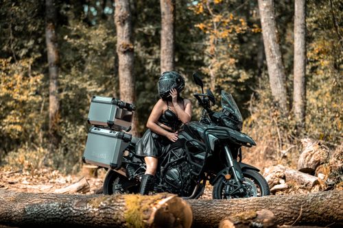 Free Woman on adventure motorcycle in forest setting, embodying freedom and exploration. Stock Photo