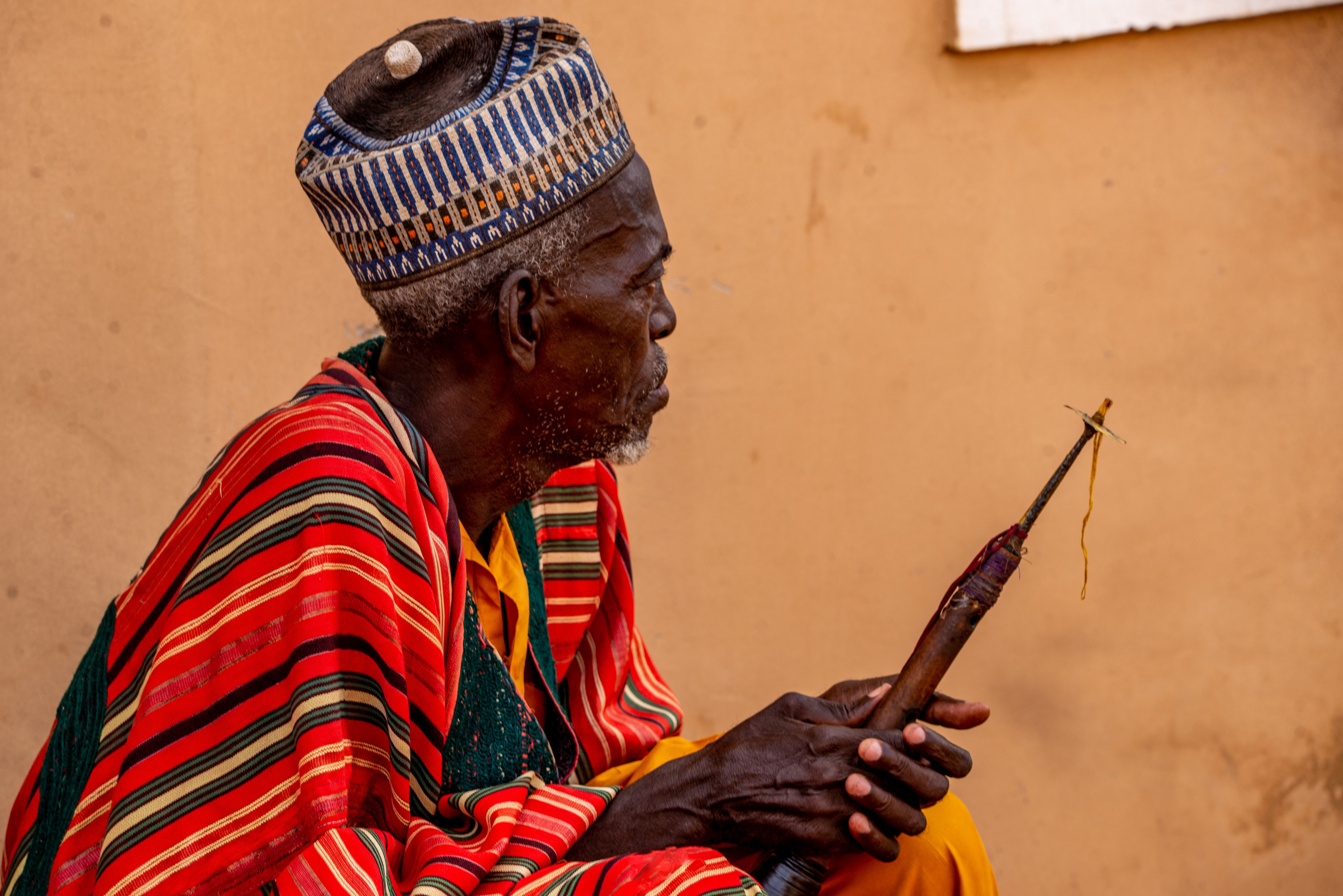 Elderly man in colorful traditional attire holding a staff, Giade, Nigeria.