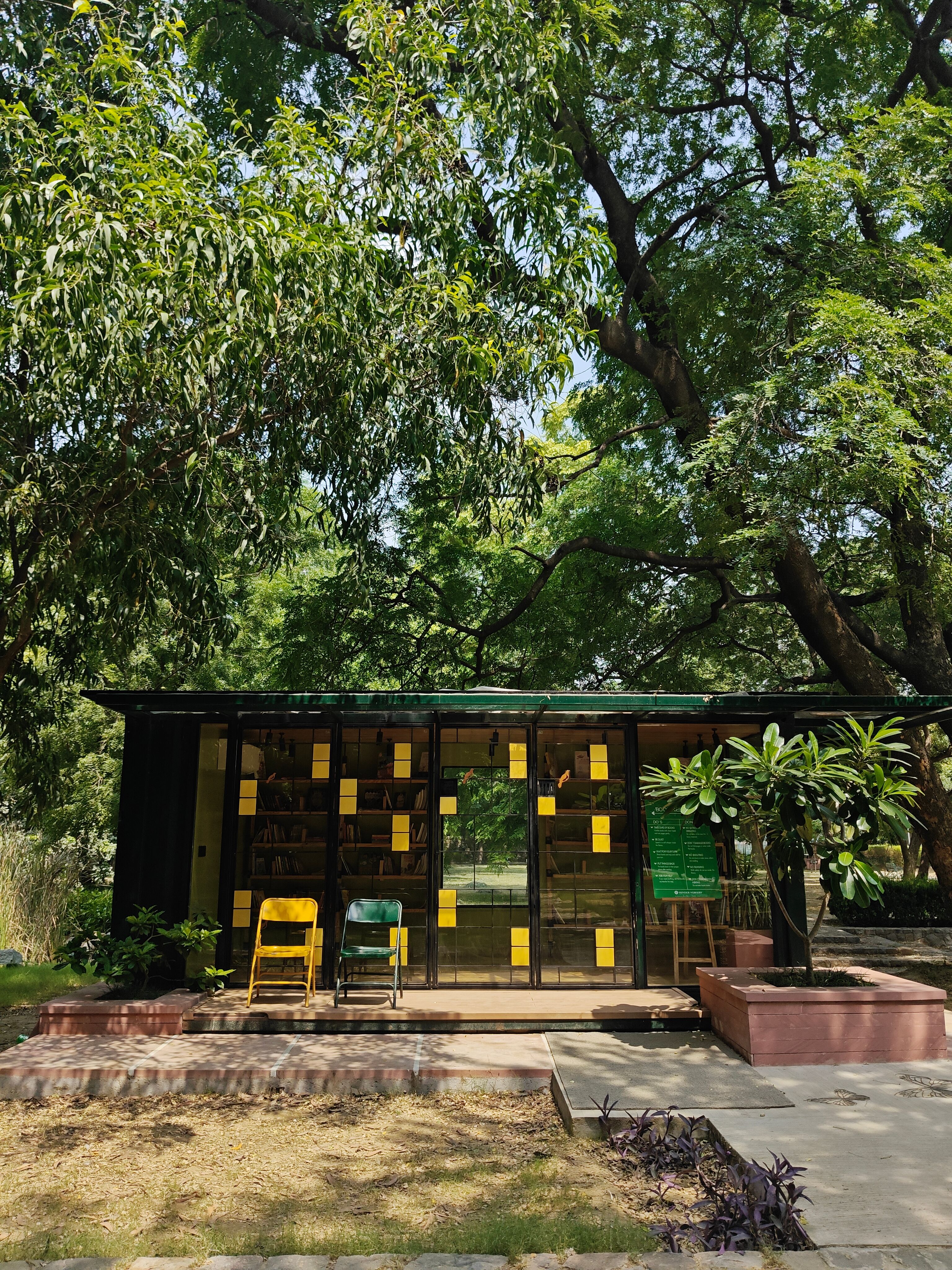 A cozy glass-front library in New Delhi's lush urban park captures serene reading moments.