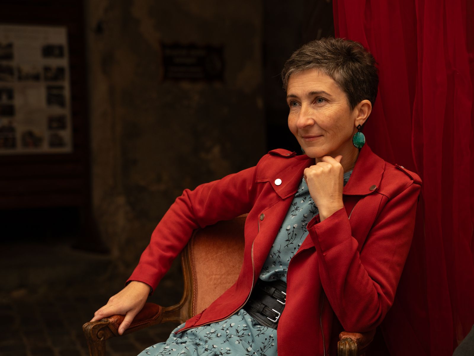 Charming portrait of a woman in red jacket sitting indoors, exuding confidence and poise.