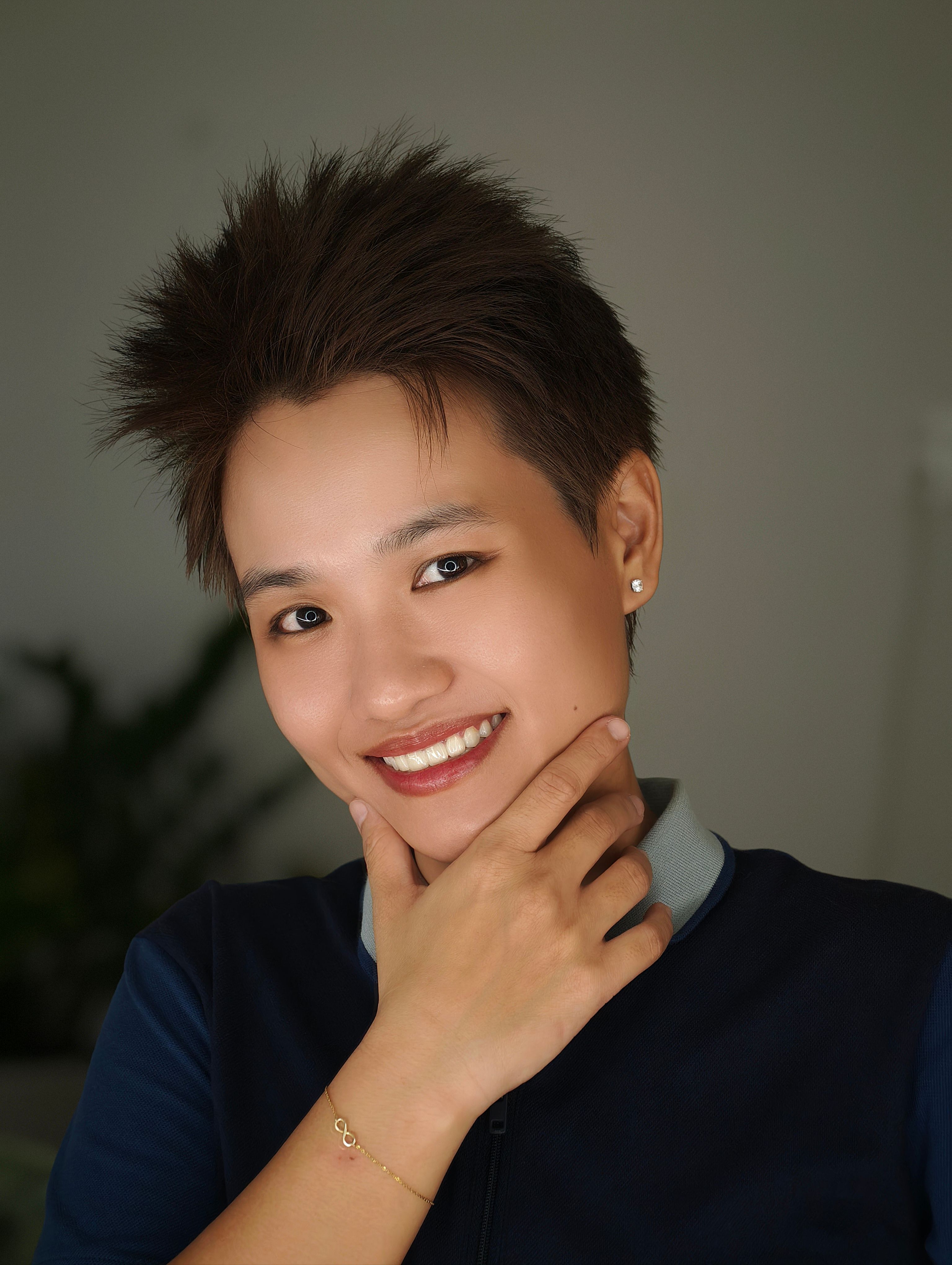 Close-up portrait of a smiling person with short spiky hair, posing indoors.