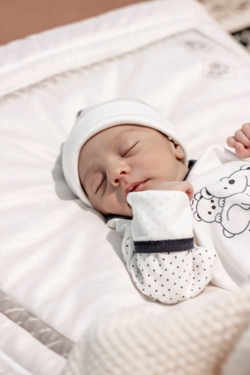 Free A serene image of a sleeping newborn baby dressed in a cute outfit, resting on a soft white blanket. Stock Photo