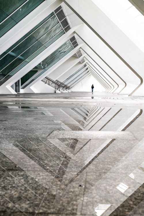 Free Striking architectural perspective with reflections and a lone figure in a modern walkway. Stock Photo