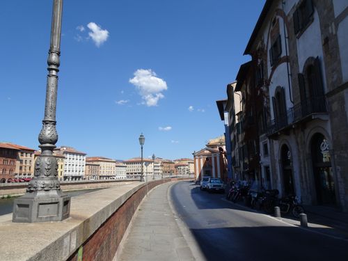 Free Street view along the Arno River in Pisa, Italy, showcasing historic architecture and vibrant skies. Stock Photo