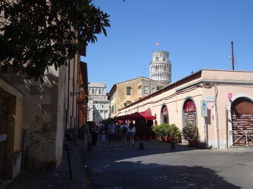 Free A vibrant street scene in Pisa featuring the iconic Leaning Tower under a blue summer sky. Stock Photo