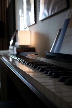 A side view of a piano keyboard with sunlight, books, and soft lighting in a cozy room.