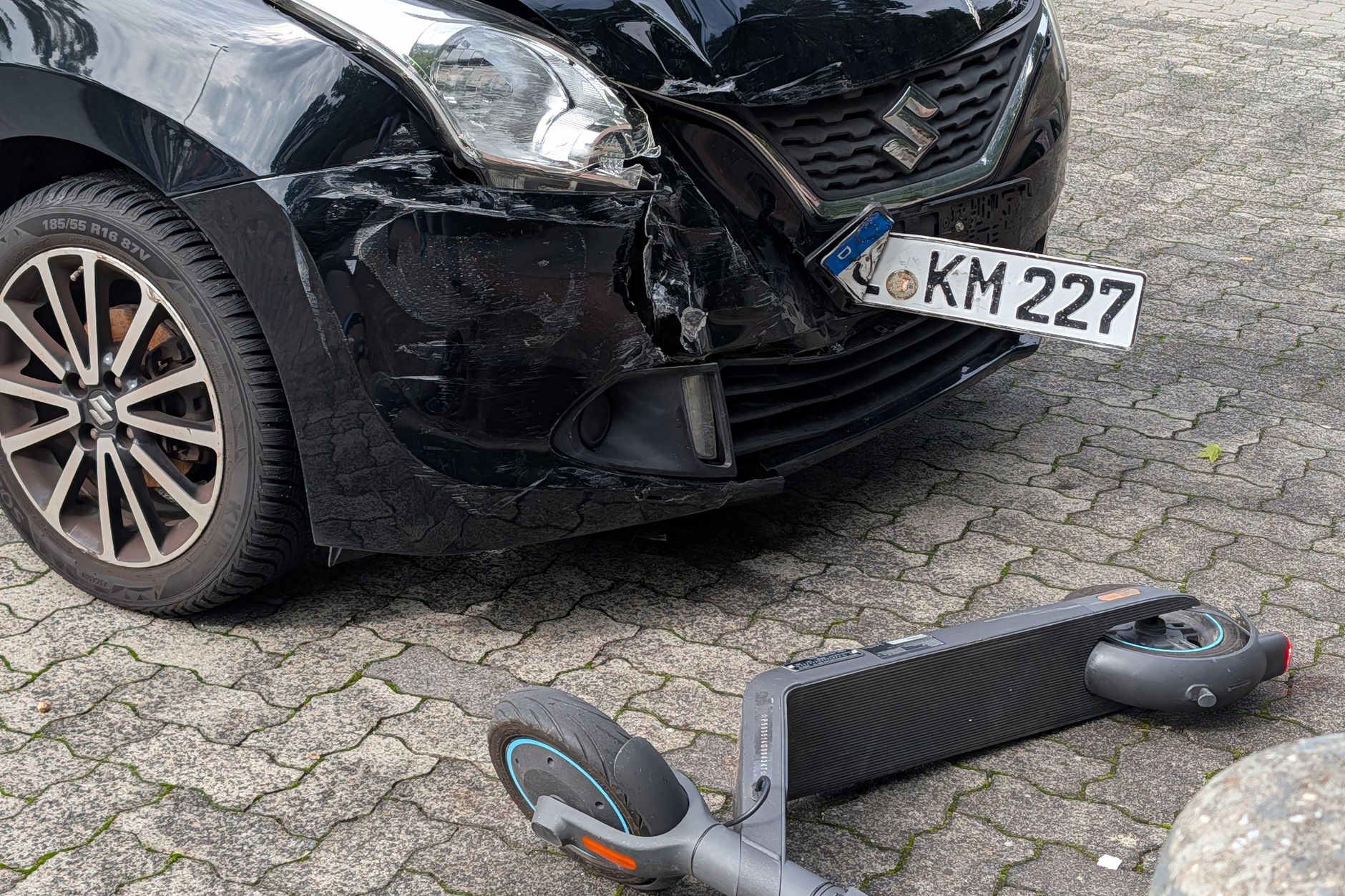 A damaged car and scooter after a collision in an urban setting.