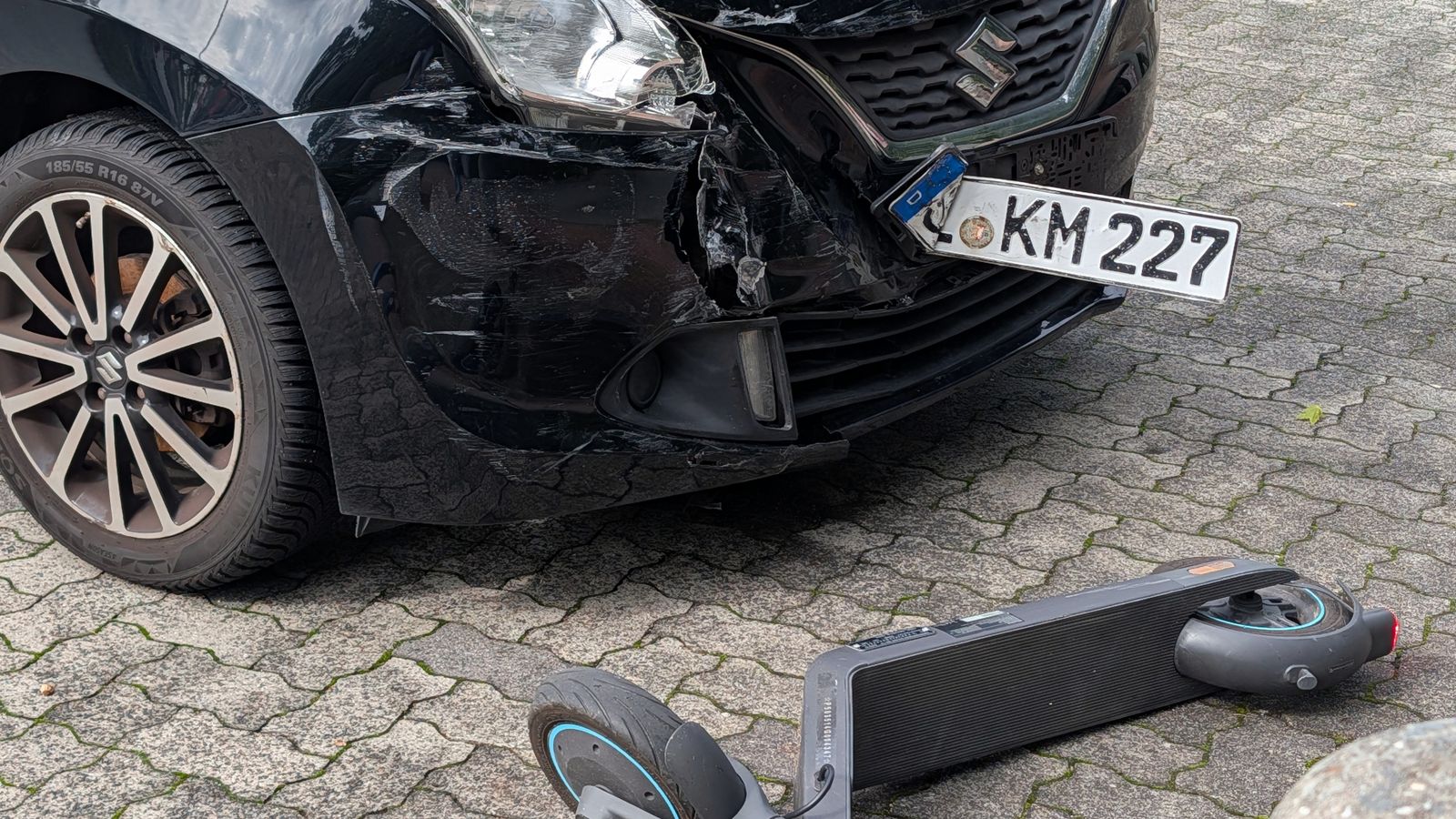 A damaged car and scooter after a collision in an urban setting.