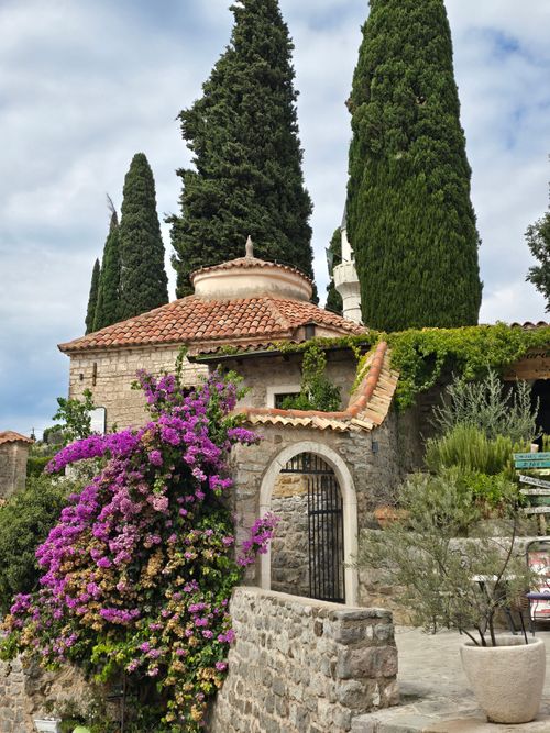 Free Charming stone villa with blooming bougainvillea and cypress trees under a cloudy sky. Stock Photo