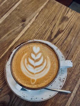 Top-down view of a latte with a heart-shaped foam art in a white cup on a wooden table.