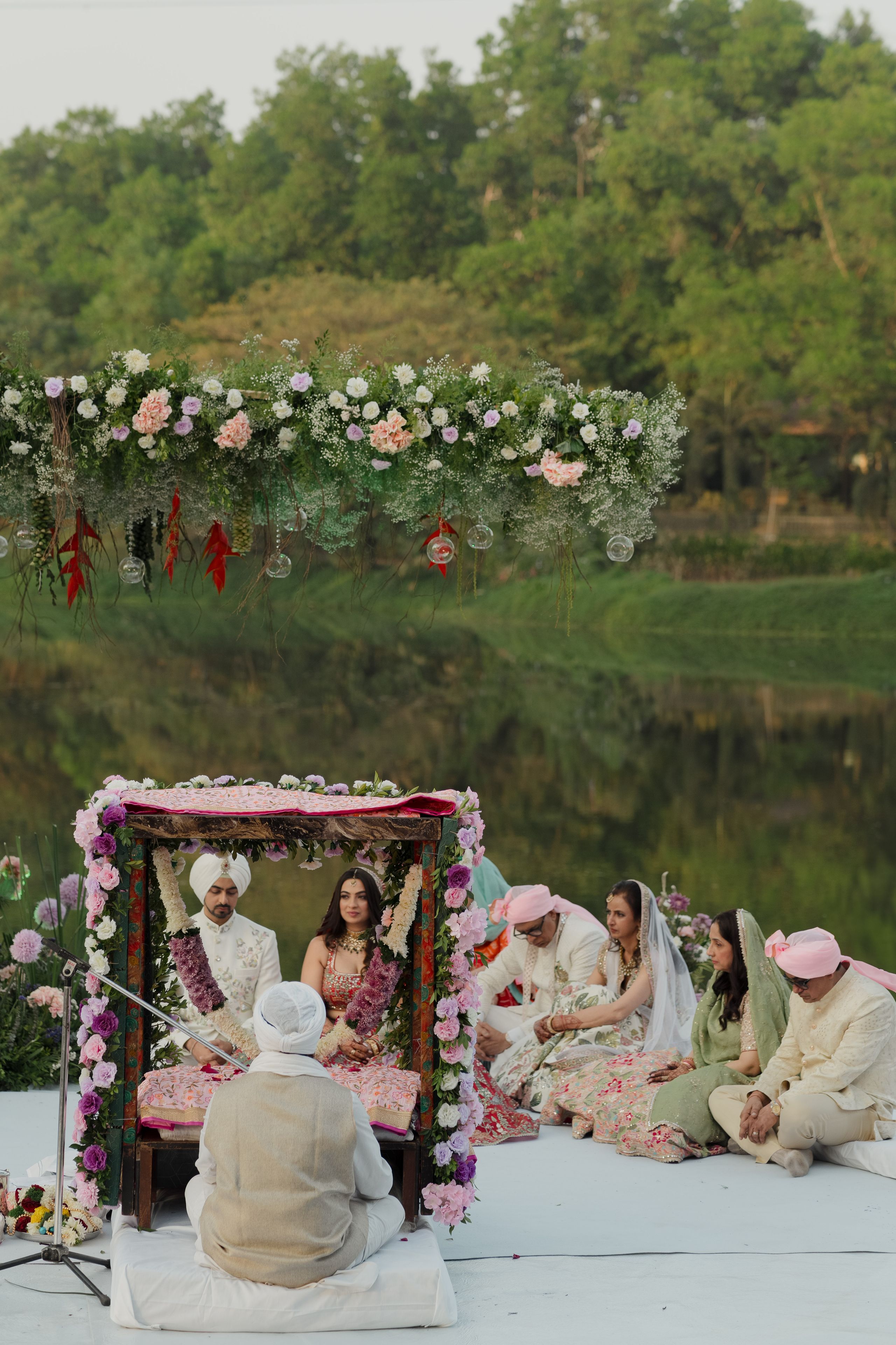 Outdoor Hindu wedding ceremony beneath a floral canopy beside a lake