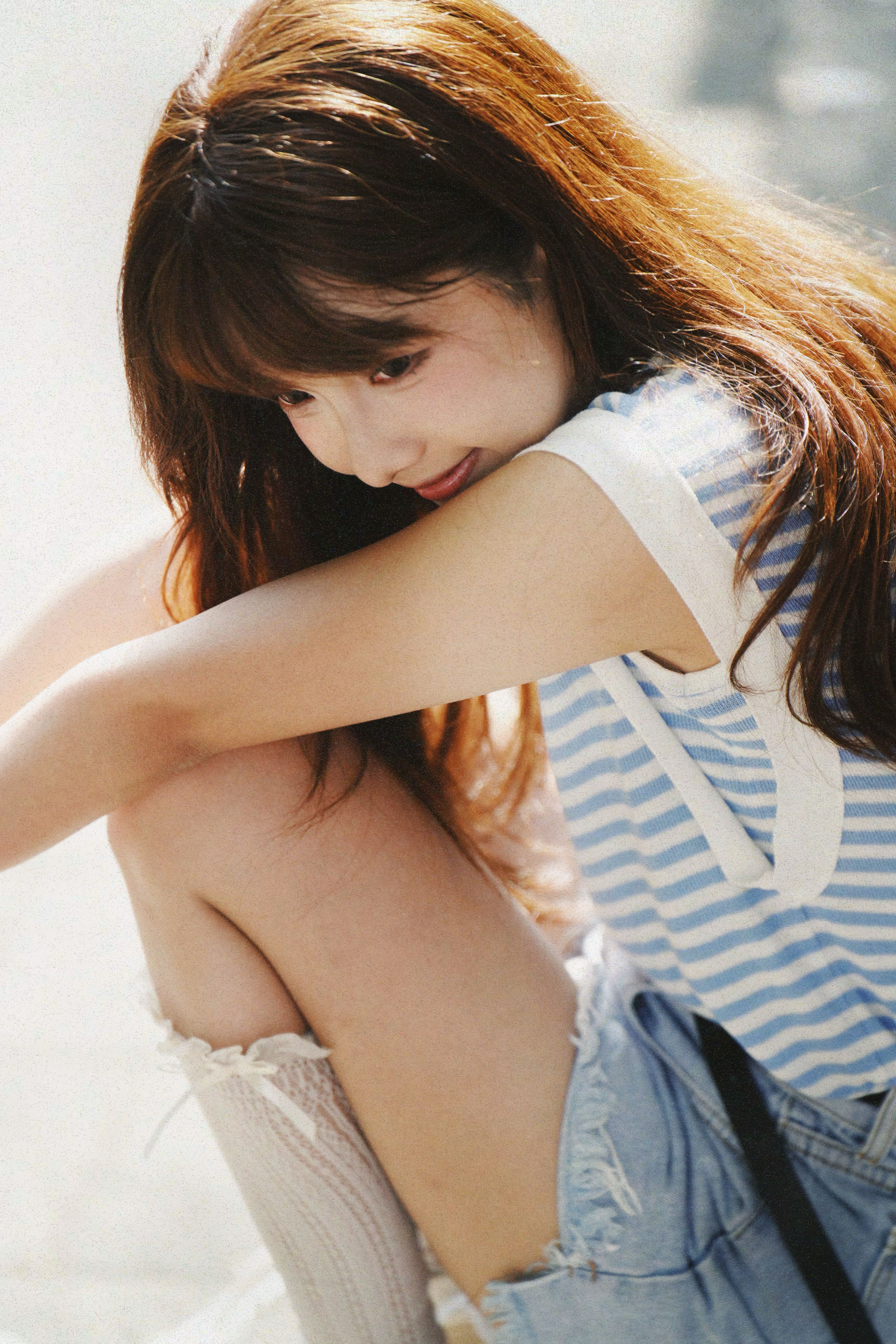 Young woman in casual summer attire sitting outdoors, looking thoughtful.