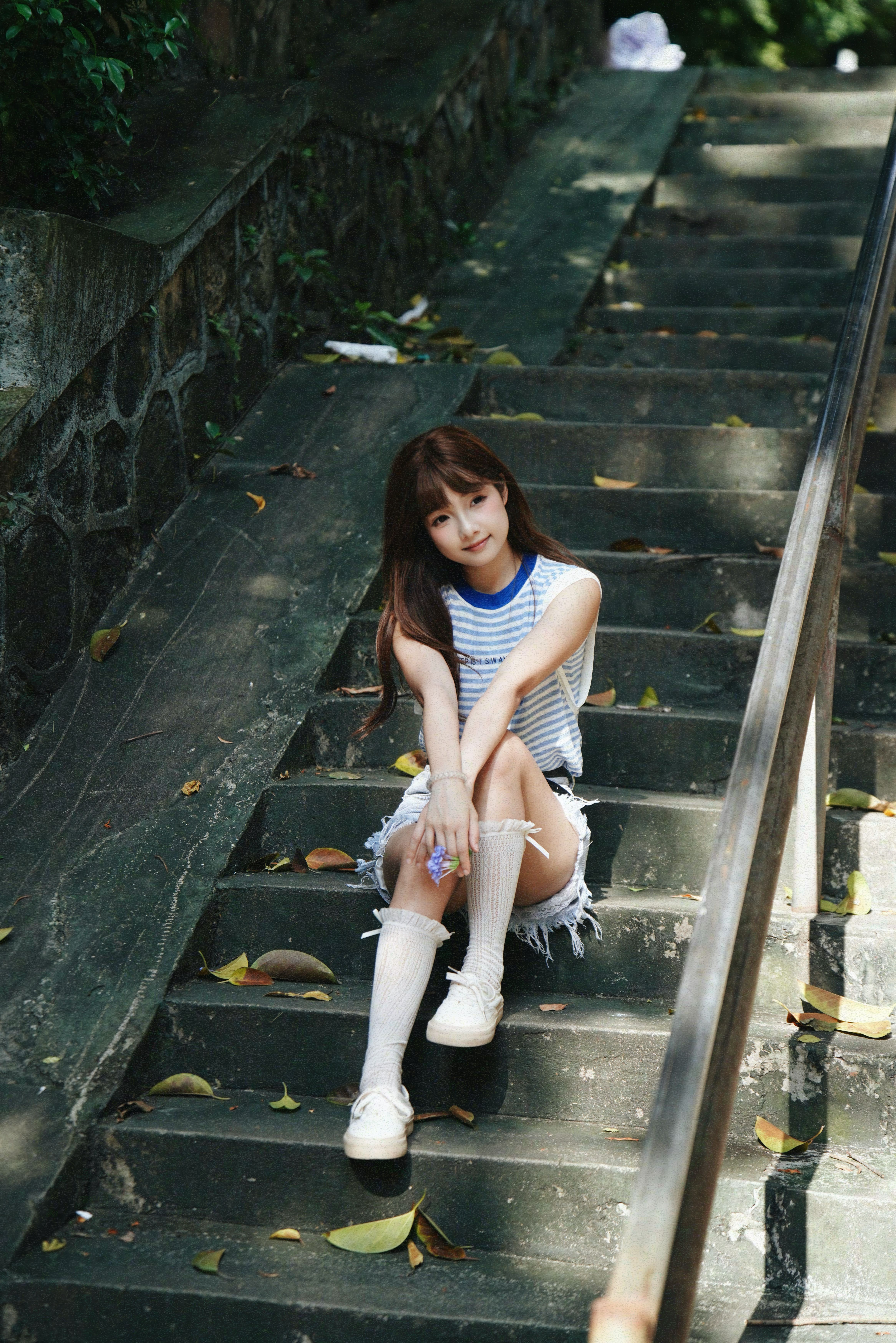 Young woman sitting on outdoor stone steps surrounded by fallen leaves.
