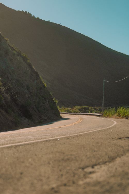 Free Winding road along a scenic mountain landscape with clear blue skies, perfect for travel and adventure imagery. Stock Photo