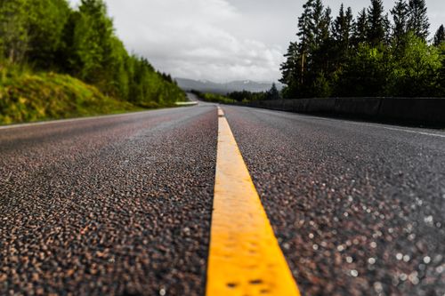 Free Lonely road in Norway surrounded by lush green forests and dramatic skies. Stock Photo