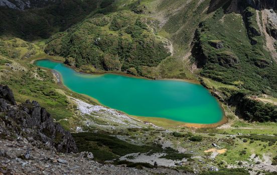 Turquoise alpine lake embraced by green vegetated mountain slopes