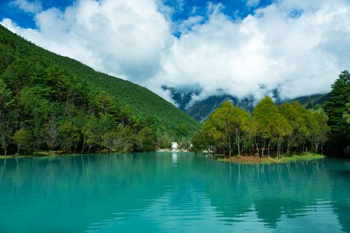 Free Breathtaking view of a turquoise lake surrounded by lush mountains and clouds in Lijiang, Yunnan, China. Stock Photo