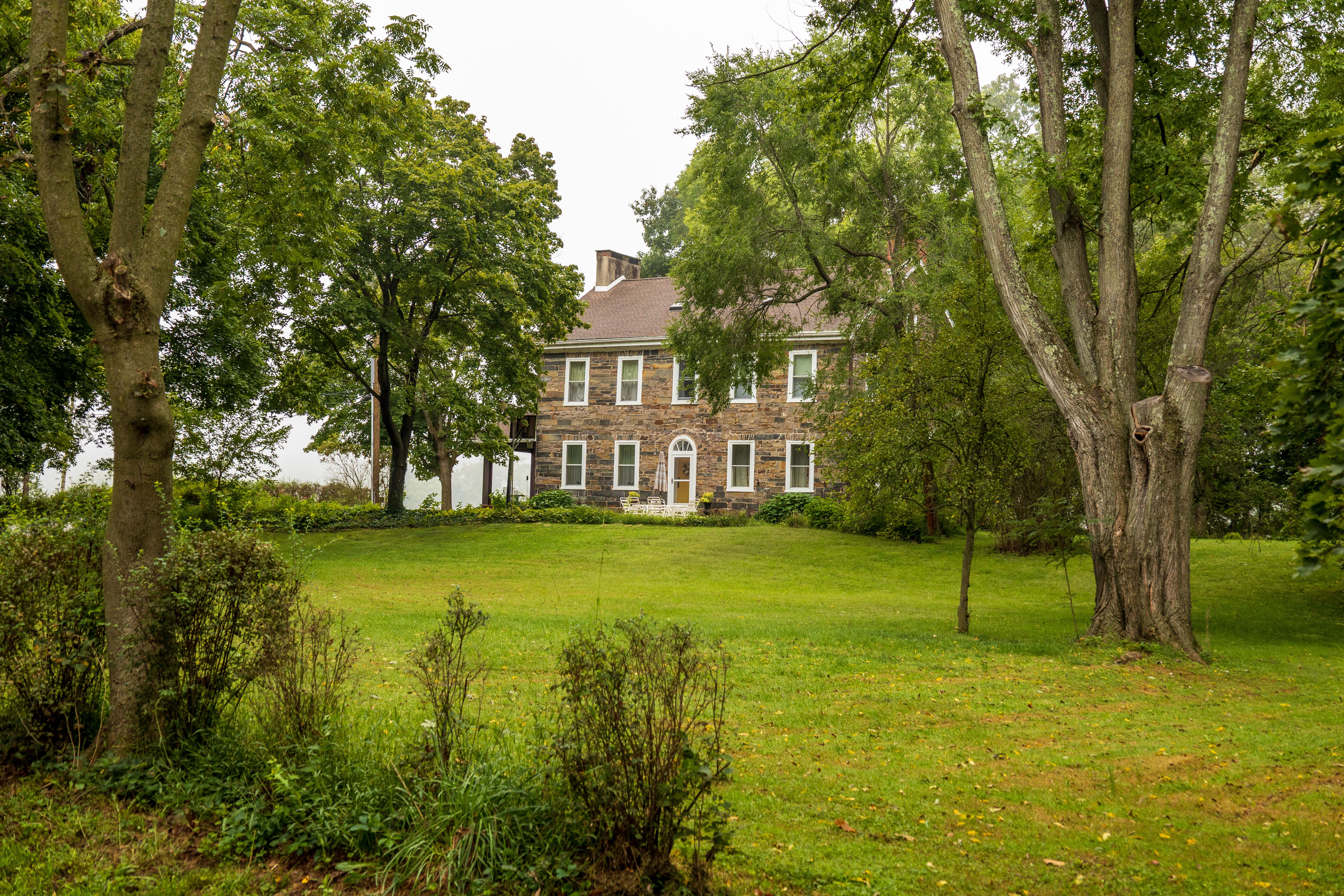 A picturesque stone house set amidst a lush green landscape with tall trees and a well-kept lawn.
