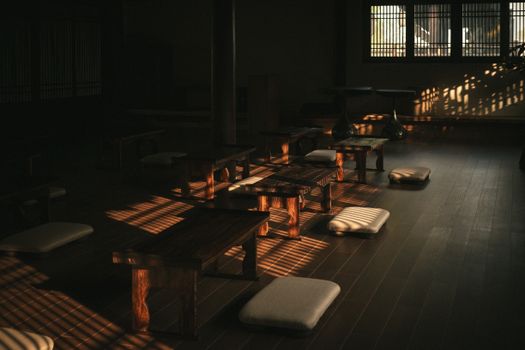Sunlit peaceful meditation room with wooden tables and cushions on a wooden floor.