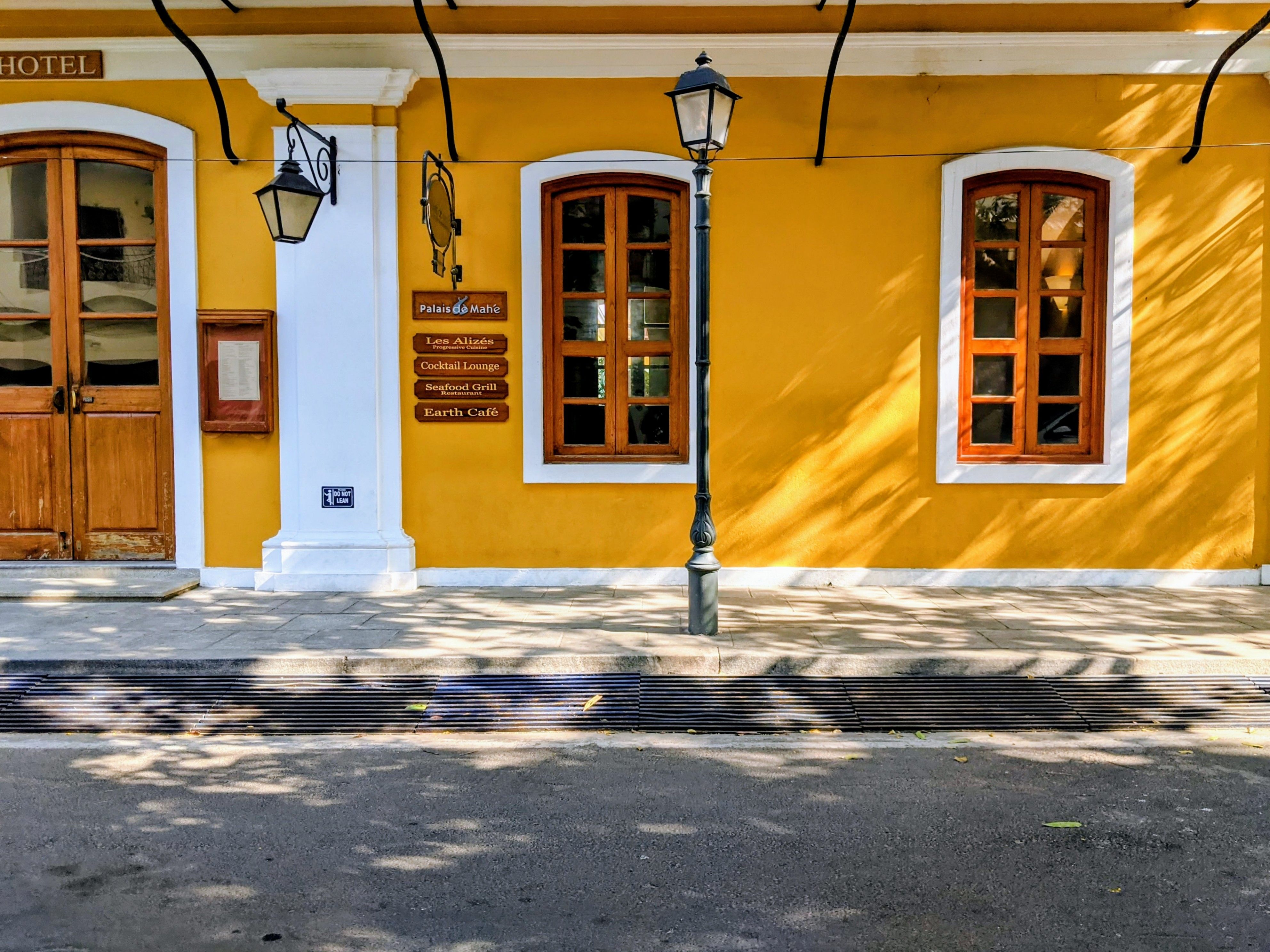 A classic yellow facade of French colonial architecture with wooden windows and street lamps.