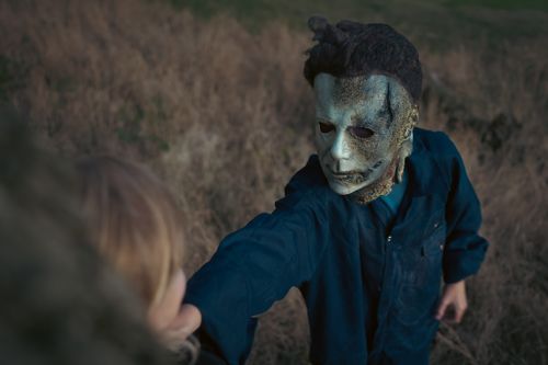Free A person in a Michael Myers mask reaches menacingly towards the camera in an autumn field at sunset. Stock Photo