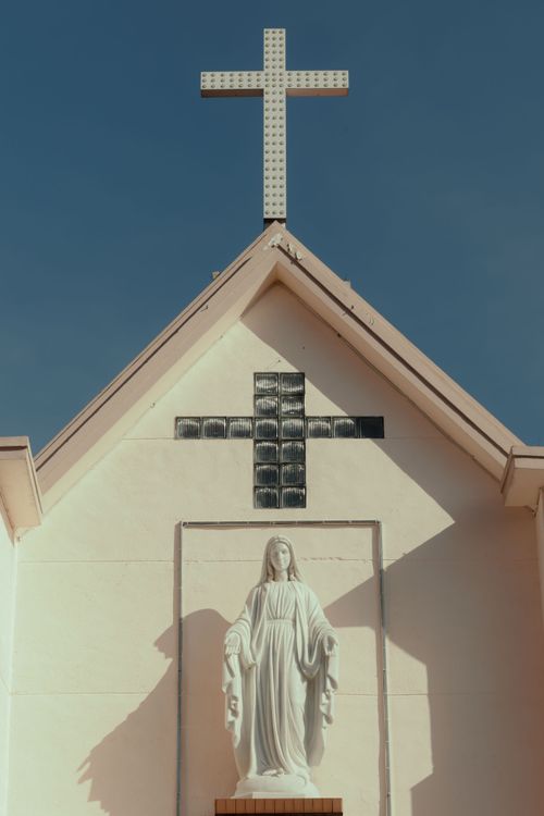 Free A church facade featuring a cross and religious statue under a clear sky. Stock Photo