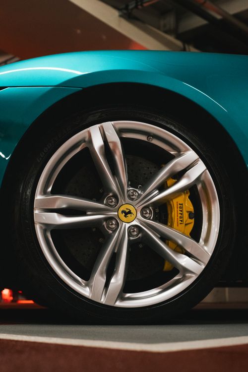 Free Detailed view of a teal Ferrari wheel and yellow brake caliper in a garage setting. Stock Photo
