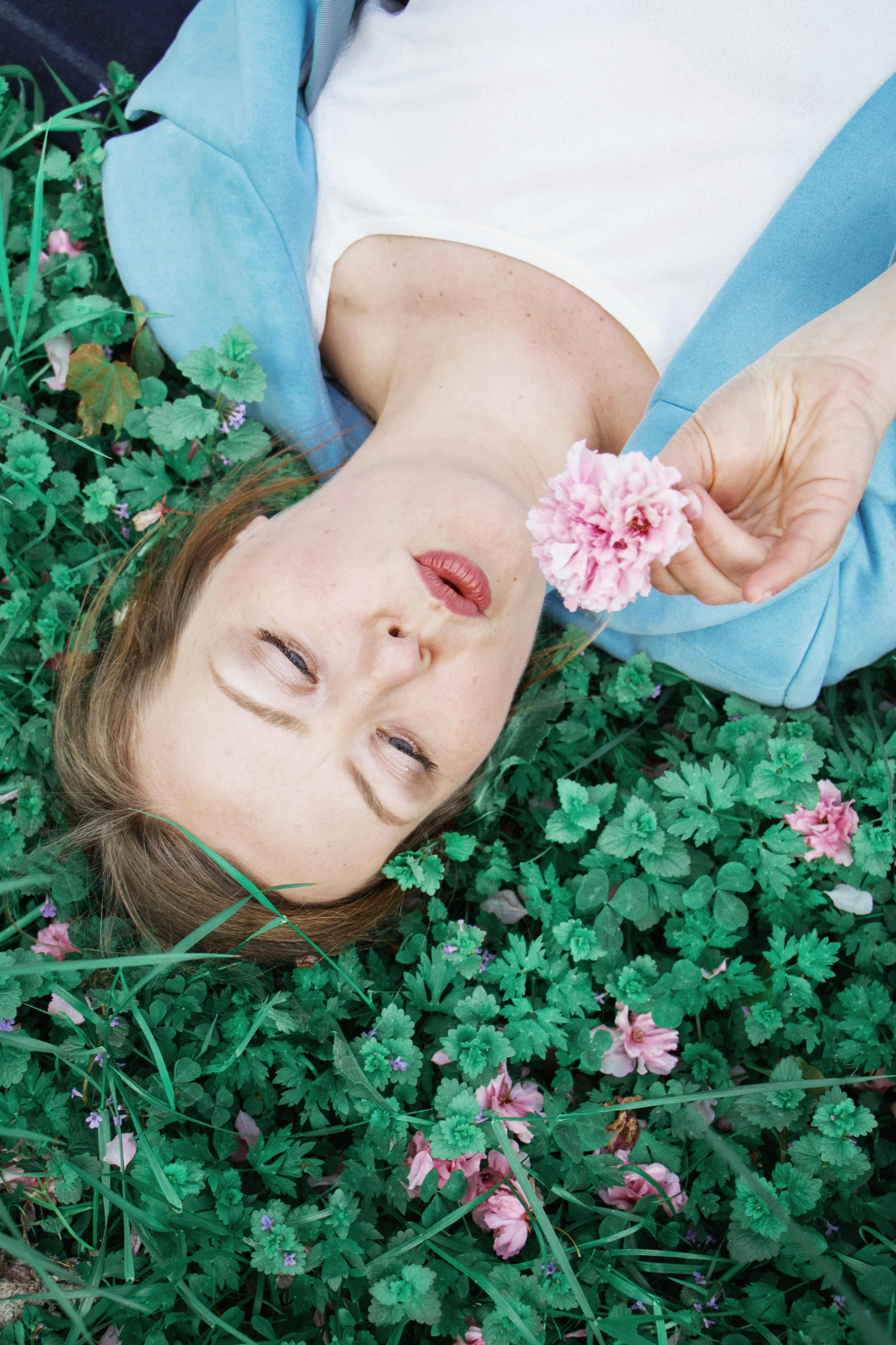 calm woman lying on grass with blooming flowers in summer