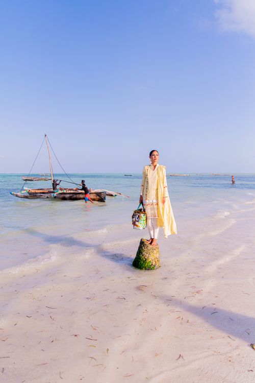 Free A woman in a yellow dress stands on a tropical beach with a Dhow boat and fisherman in Zanzibar. Stock Photo