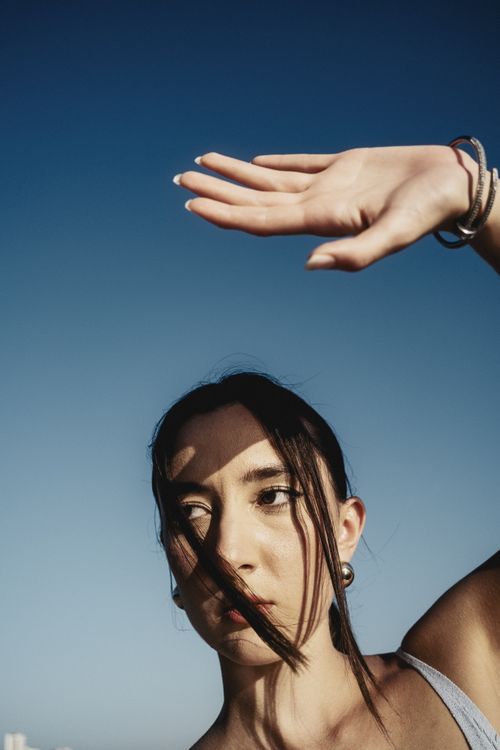 Free A woman shields her eyes from sunlight with her hand against a clear blue sky. Stock Photo