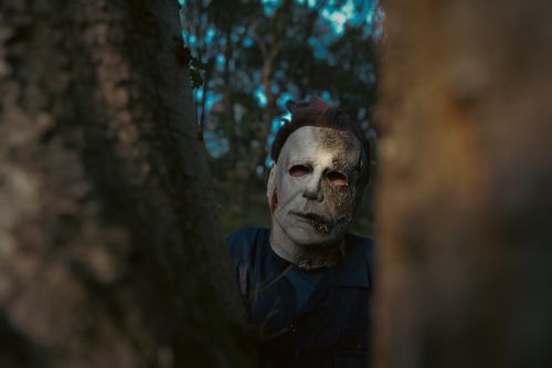 Free A chilling masked character lurks in a dark forest, embodying a horror movie atmosphere. Stock Photo