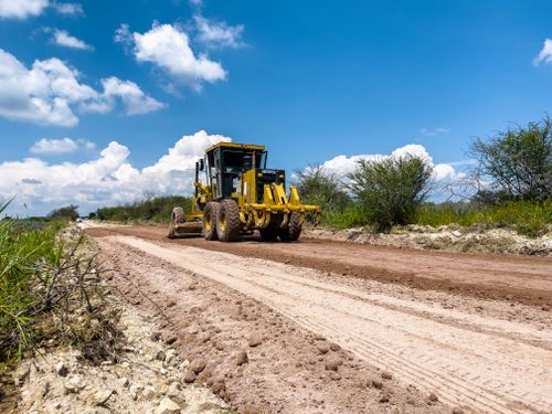 Free A yellow bulldozer working on a dirt road under a bright blue sky with clouds. Stock Photo