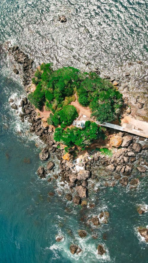 Free Stunning aerial view of a small rocky island with lush greenery surrounded by ocean waves. Stock Photo