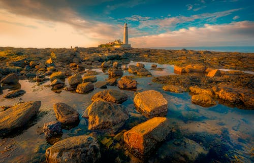 White Lighthouse On Rocky Shore Under Blue Sky