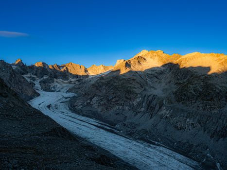A stunning view of Bregaglia Valley with sunlit peaks and a glacier at sunrise in Graubünden, Switzerland.