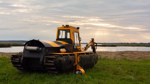 Free Yellow tractor on the grassy shores of Bраслав Lake, Belarus during sunset. Peaceful landscape scene. Stock Photo
