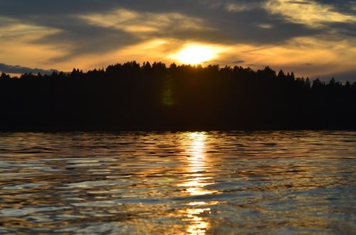 Free A tranquil sunset reflects beautifully over a calm lake with silhouetted trees on the horizon. Stock Photo