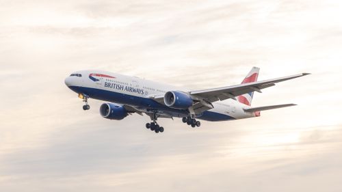 Free British Airways jet airplane descending against a stunning sunset sky, showcasing aviation splendor. Stock Photo