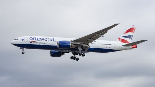 Free British Airways Boeing 777 jet airliner flying against a cloudy sky in England. Stock Photo