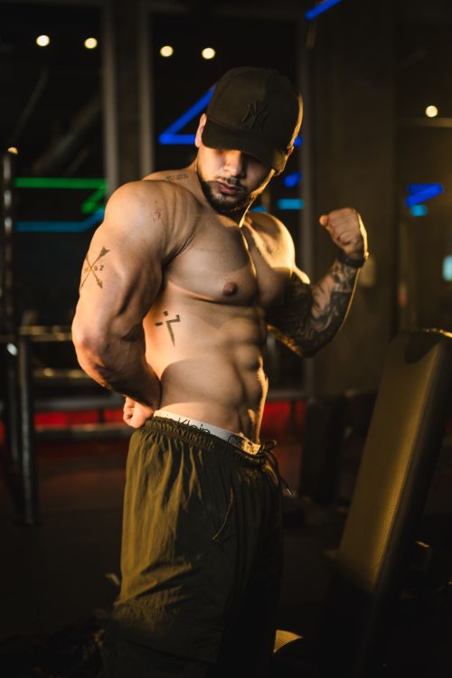 Free A male bodybuilder flexes his muscles in a gym setting, showcasing a strong physique. Stock Photo