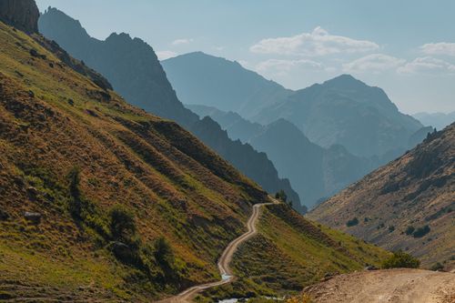 Free A breathtaking mountain road winds through scenic, rugged terrain under a bright sky. Stock Photo
